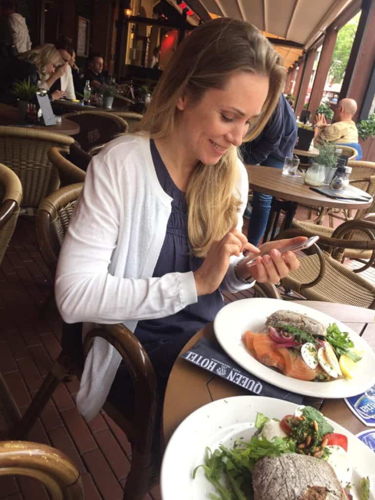 About Me photo. Elena Elliott having lunch outside looking at her phone and smiling