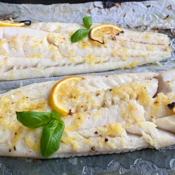 two filets of baked blue grenadier served with fresh basil and lemon slices