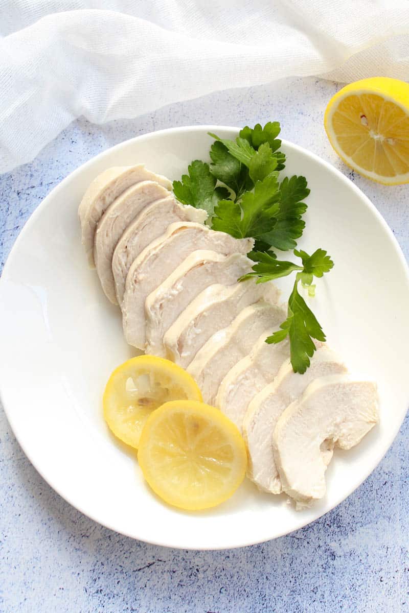 poached chicken sliced into slices, served with lemon and fresh parsley leaves