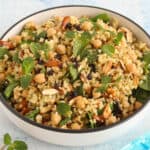 Cauliflower tabbouleh served in a white bowl, topped with fresh mint and cranberries.
