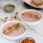 Pink roasted cauliflower soup in two bowls with roasted chickpeas