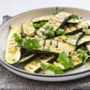 grilled zucchini slices on a white plate served with cilantro leaves