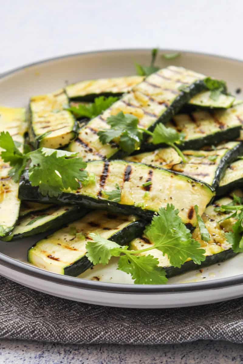 grilled zucchini slices on a white plate with coriander leaves