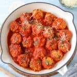 Chicken meatballs simmering in tomato sauce inside a white frying pan, ready to be served as a hearty meal.
