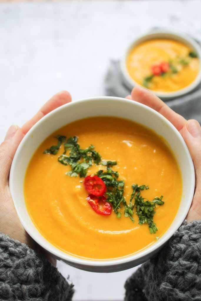 bowl of orange soup held between two hands