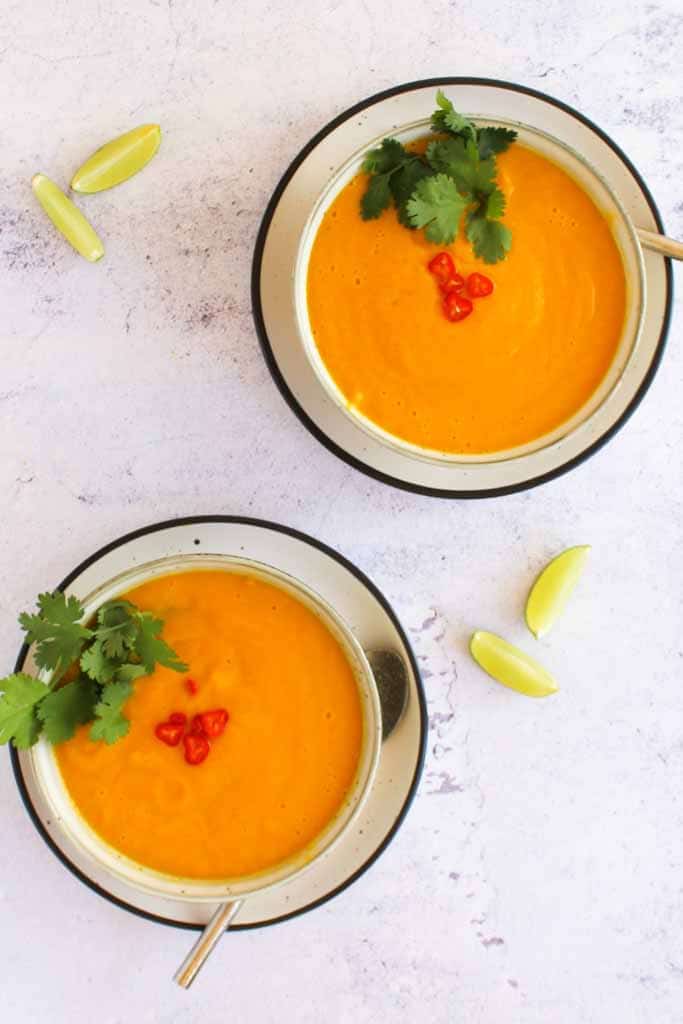 two bowls of orange carrot soup garnished with coriander 