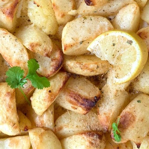 roast potatoes on a tray with lemon wedge and small coriander leaves
