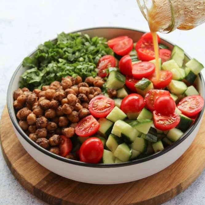 diced tomatoes, cucumber and spiced chickpeas in a plate , dressing is poured over the salad