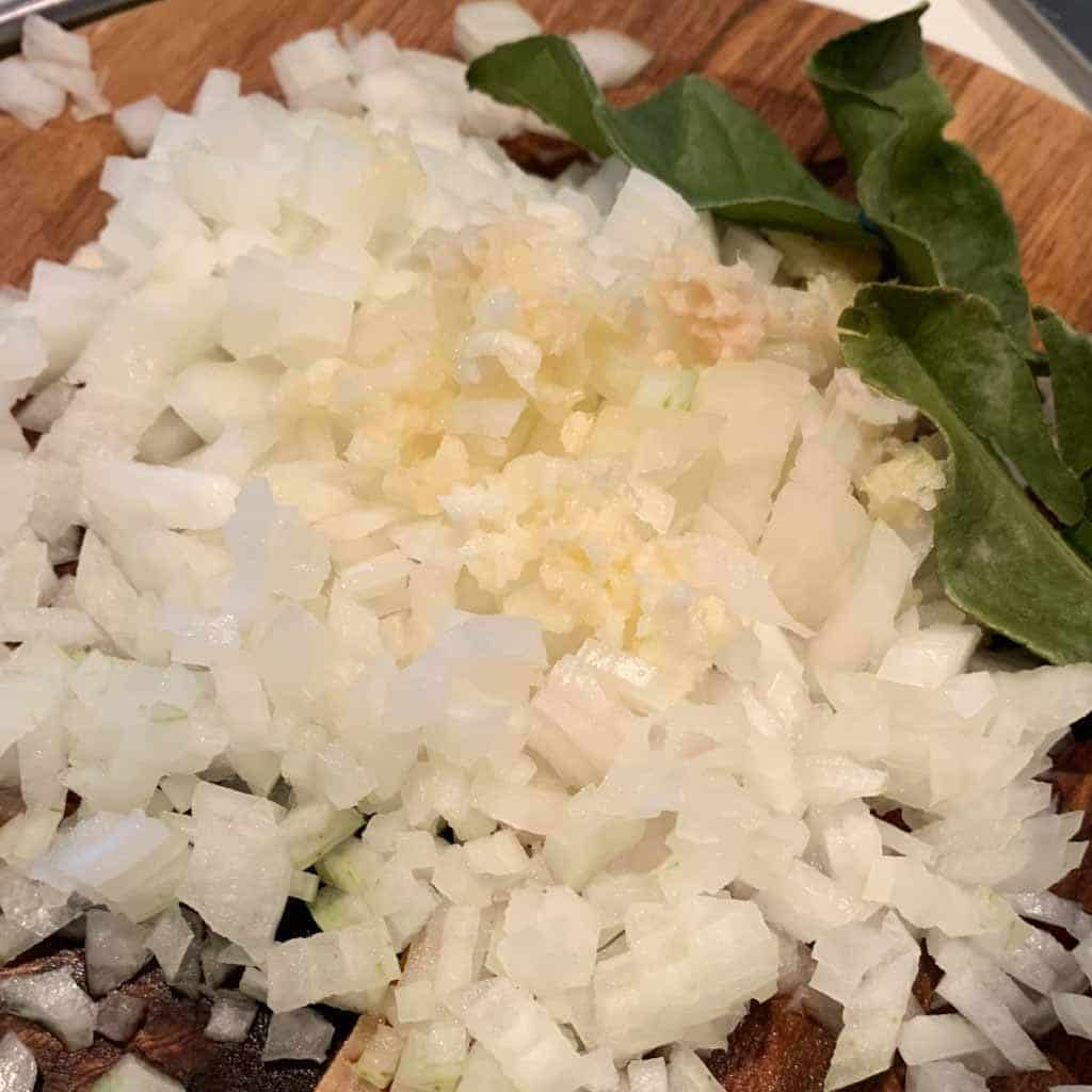 chopped onions, garlic and ginger on a wooden chopping board