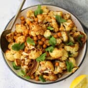 roasted cauliflower and chickpeas in a white plate served with fresh coriander and lemon