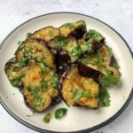 roasted eggplant slices on a plate with fresh chopped coriander