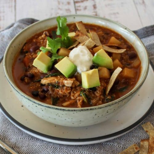 Mexican soup with black beans and shredded chicken garnished with sour cream and coriander