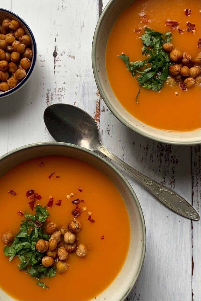 two bowls of very bright orange carrot and potato soup served with roasted chickpeas and fresh coriander