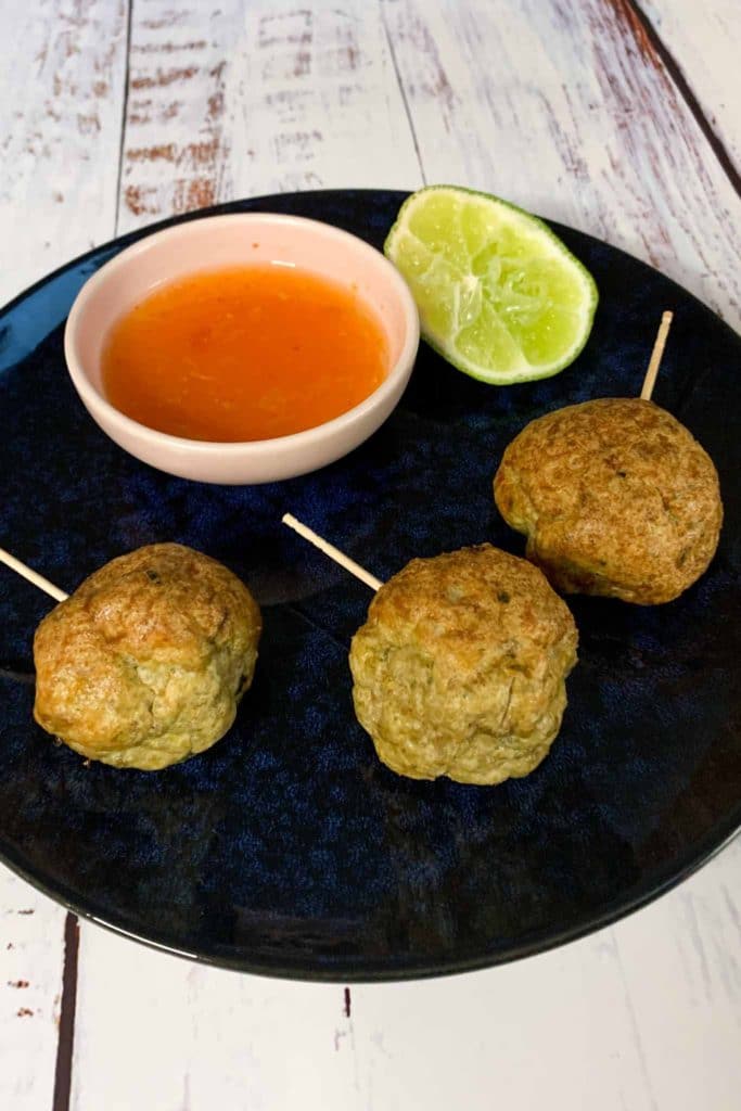 three chicken meatballs on a blue plate with dipping sauce and lime wedge