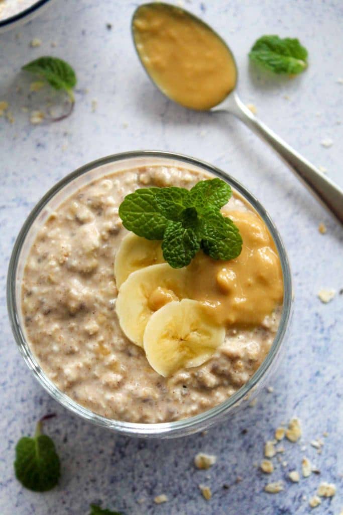 banana and peanut butter overnight oats in a glass cup with banana slices and dollop of peanut butter, photo from above