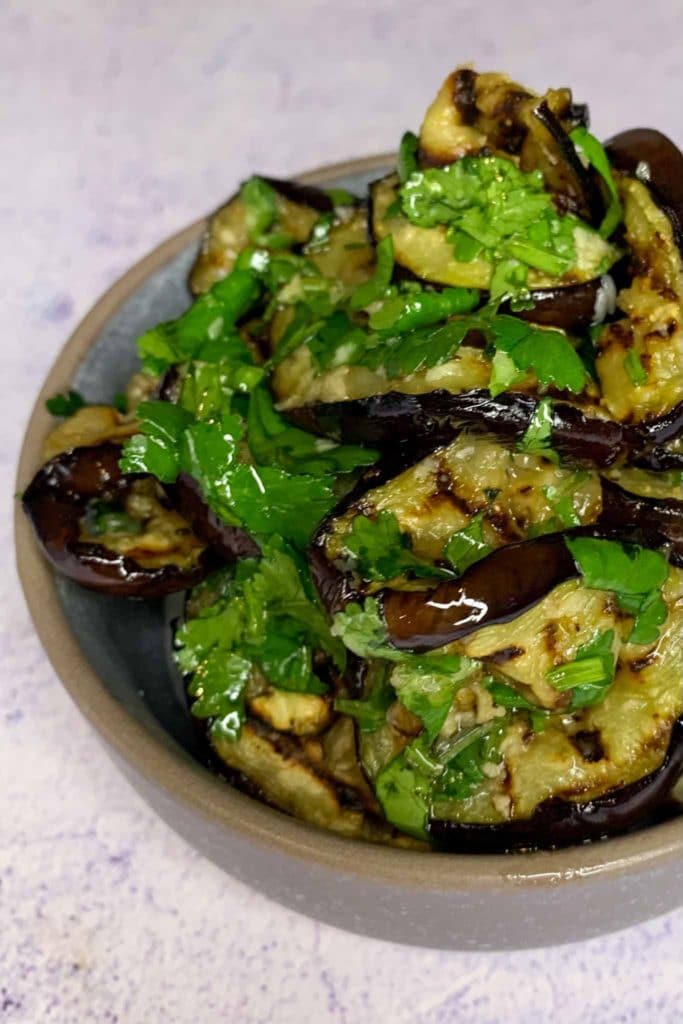 slices of grilled eggplant with parmesan and coriander leaves and olive oil in a small grey bowl