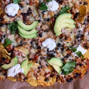 baked nachos with chicken, black beans, sour cream and avocado on a baking tray