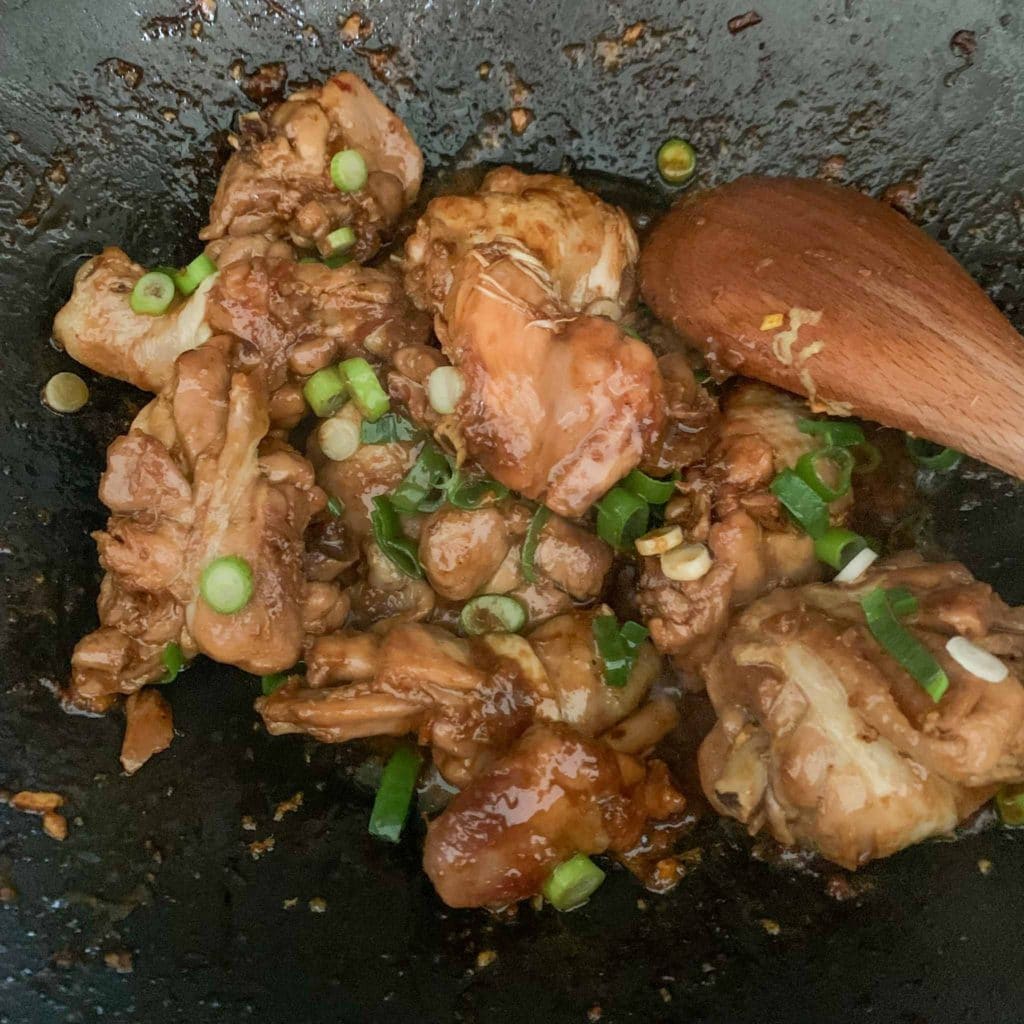 chicken pieces in a wok with green onions