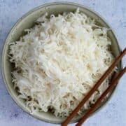 A bowl of perfect basmati rice sits fluffy and inviting in a green bowl, accompanied by a pair of wooden chopsticks against a light-colored background.