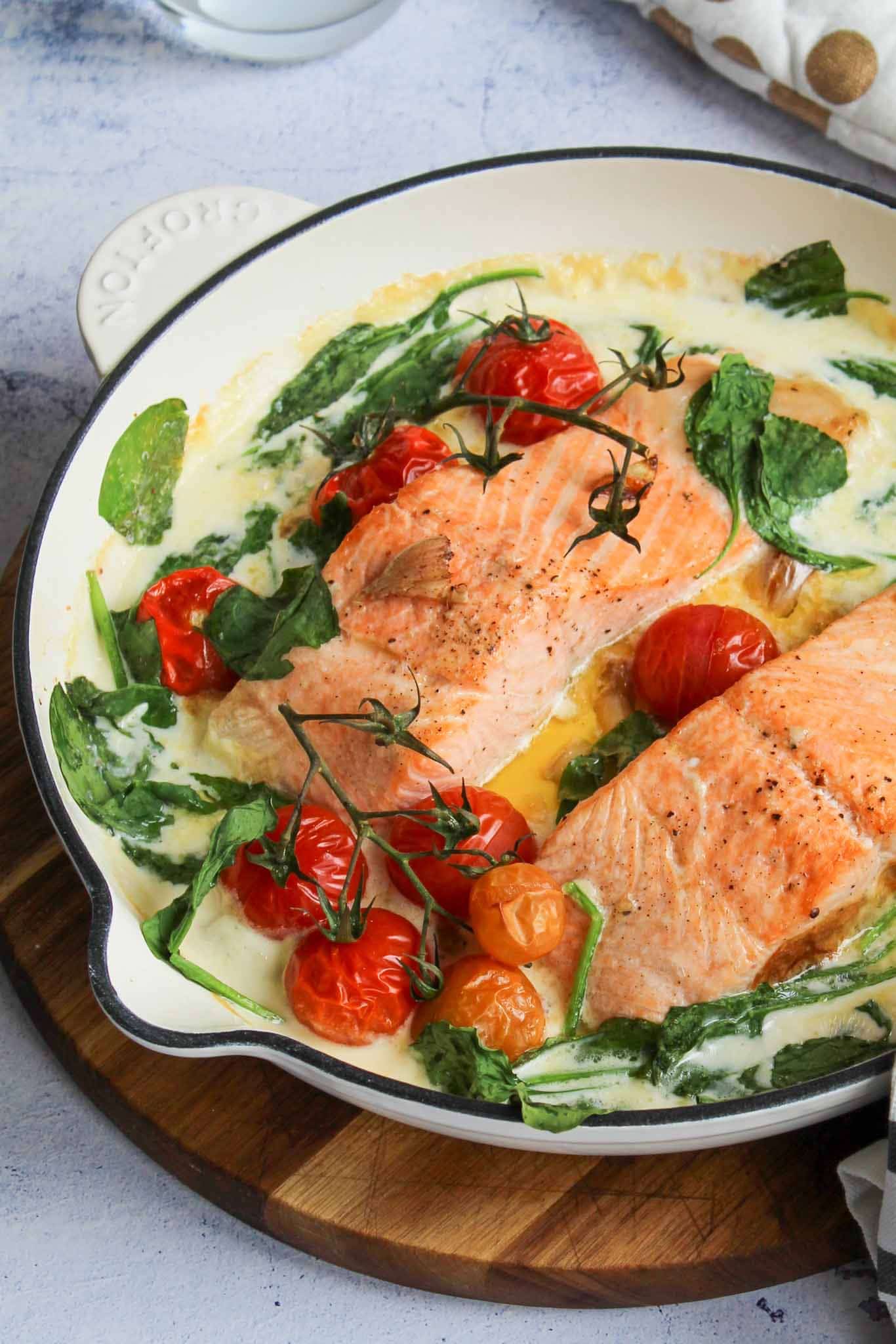 two salmon fillets cooked in creamy sauce with cherry tomatoes and spinach