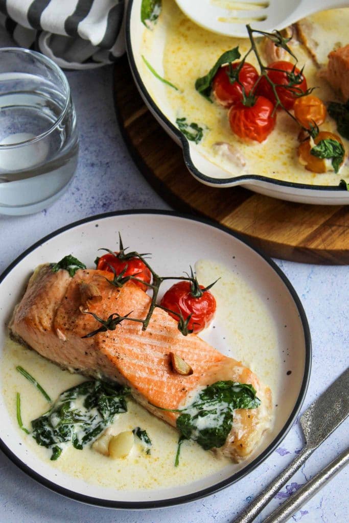 baked salmon fillet served with roasted tomatoes and spinach with a white frying pan in the background