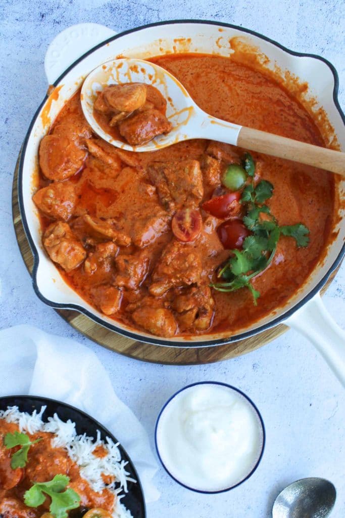 cooked butter chicken in a white Dutch oven with tomatoes and coriander as garnish 