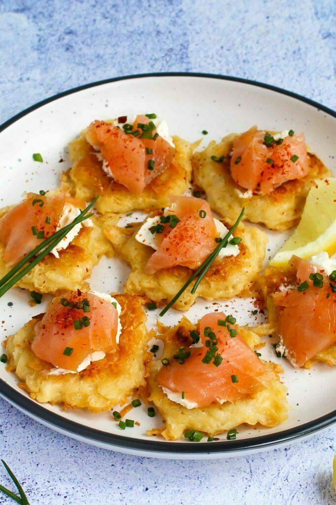 potato fritters with cream cheese and smoked salmon, served on a white plate, sprinkled with chives