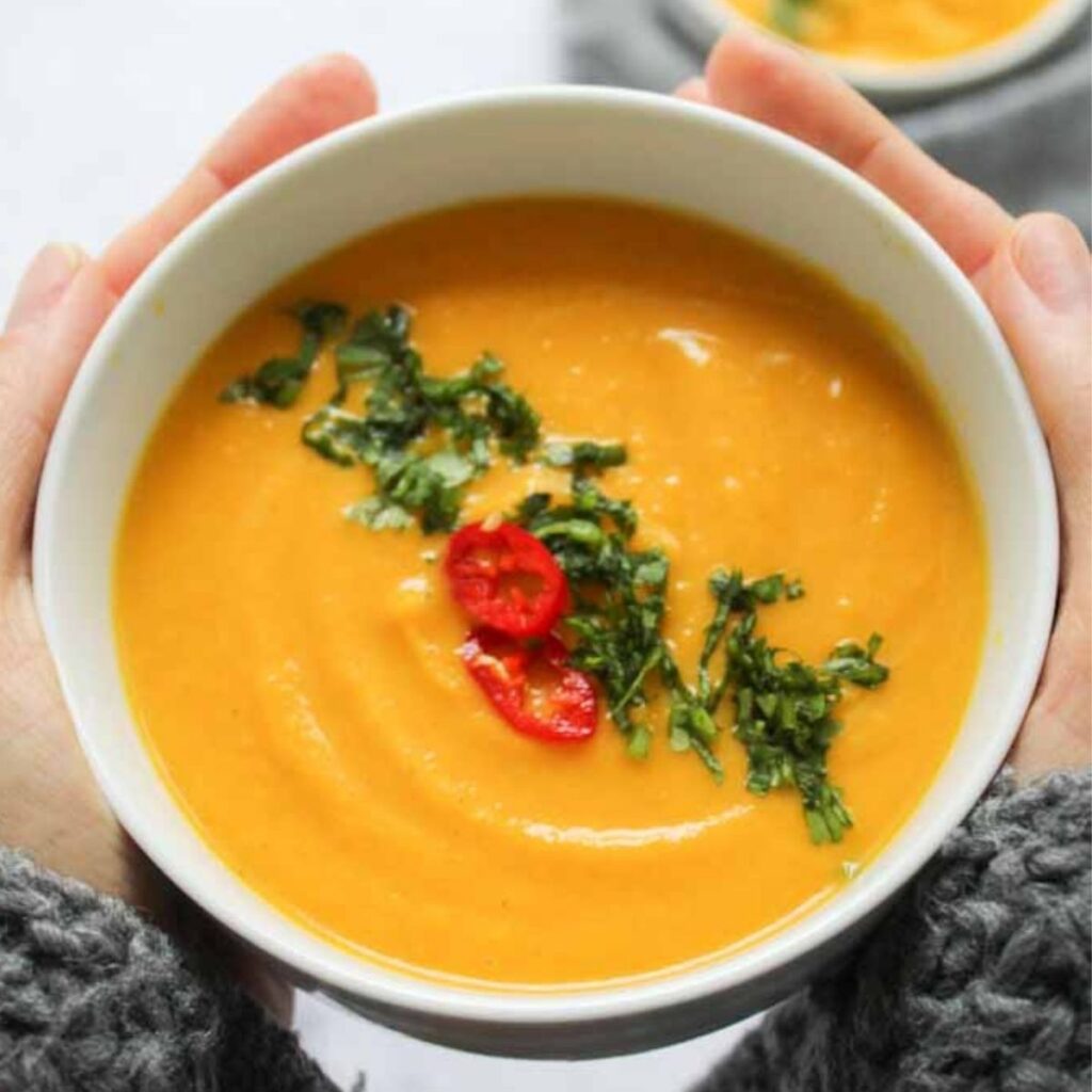 two hands holding a bowl of carrot soup