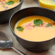 creamy pumpkin soup in black glass bowl garnished with cilies and cilantro