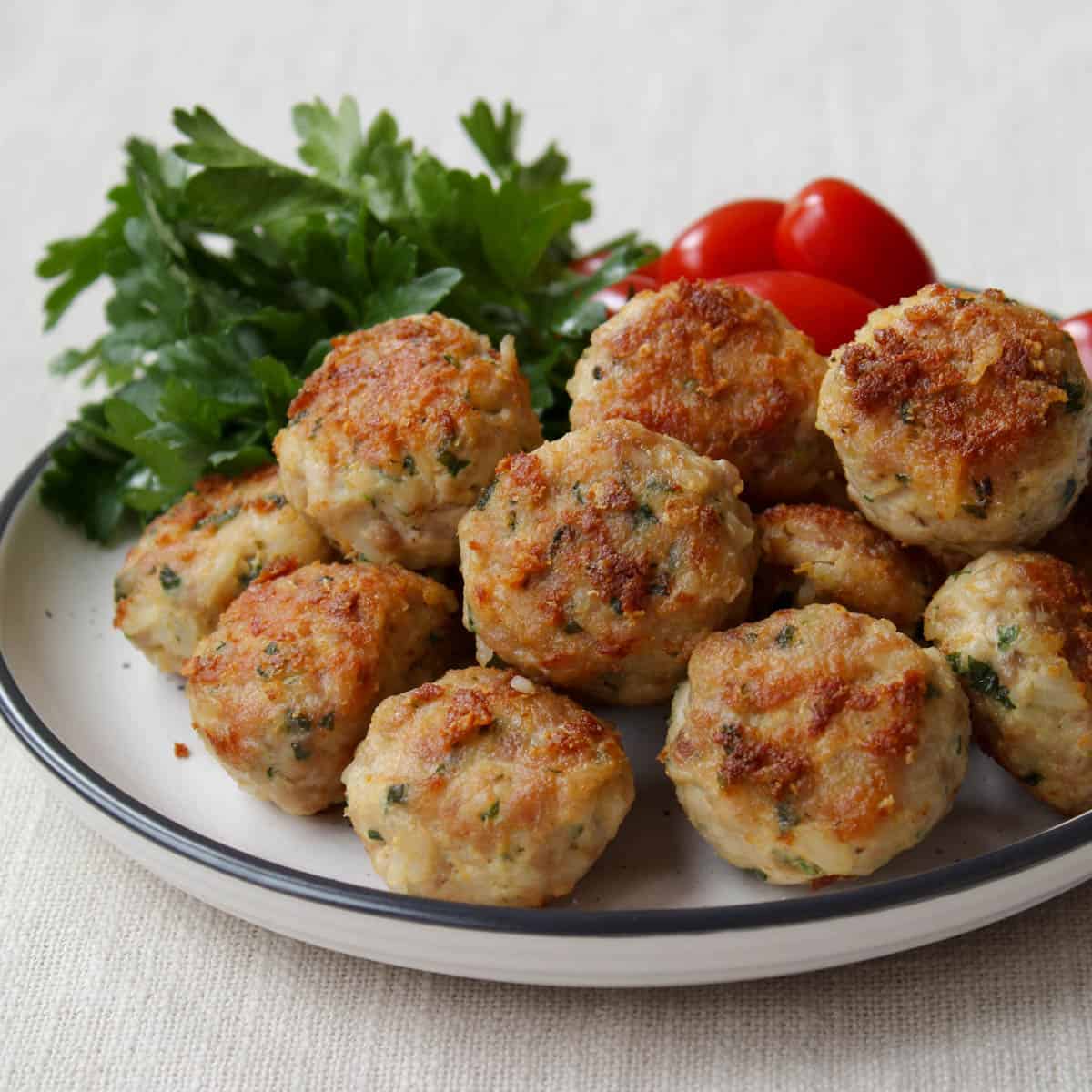 chicken meatballs on a plate with tomatoes and fresh parsley