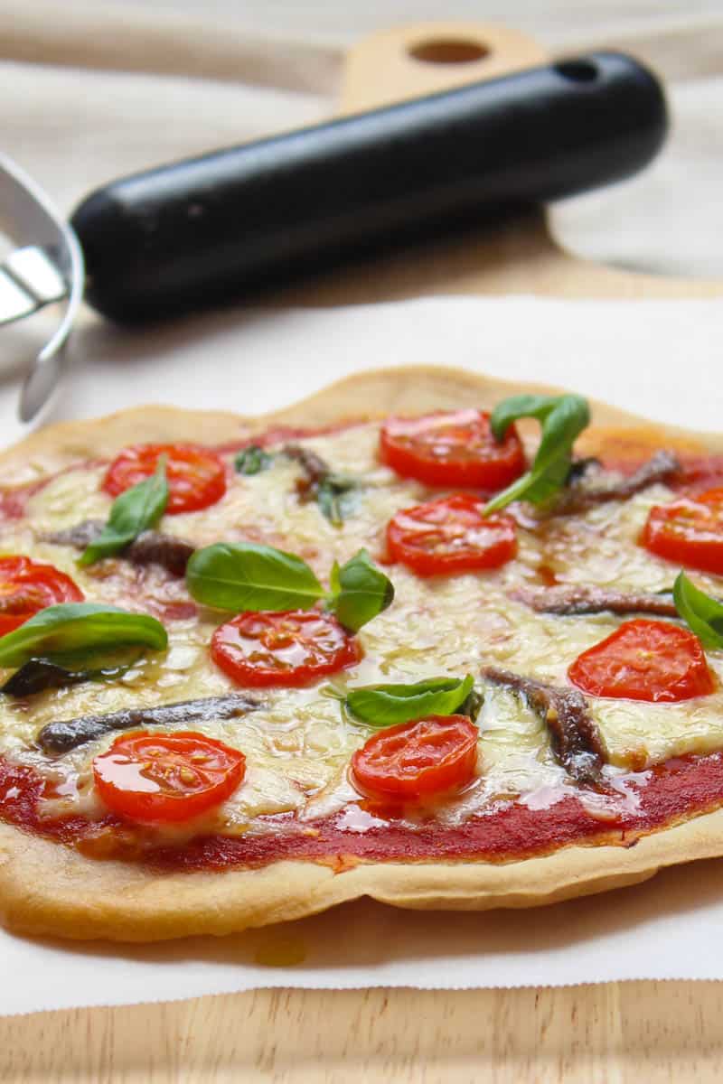 buckwheat pizza topped with tomatoes, anchovies and fresh basil leaves