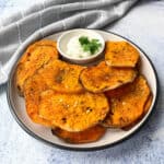 Perfectly baked sweet potato slices with a crispy golden finish, served on a plate with a dipping sauce.