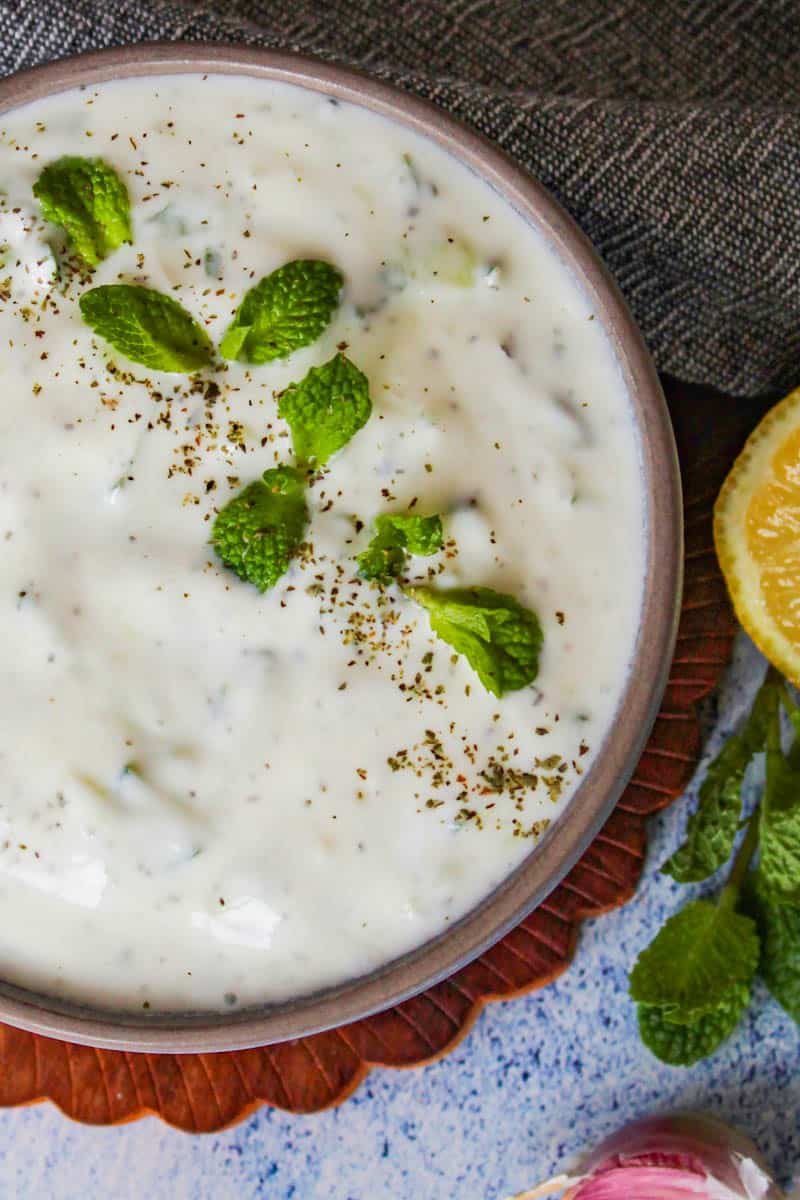 cacik Turkish yogurt dip in a brown bowl served with mint and lemon