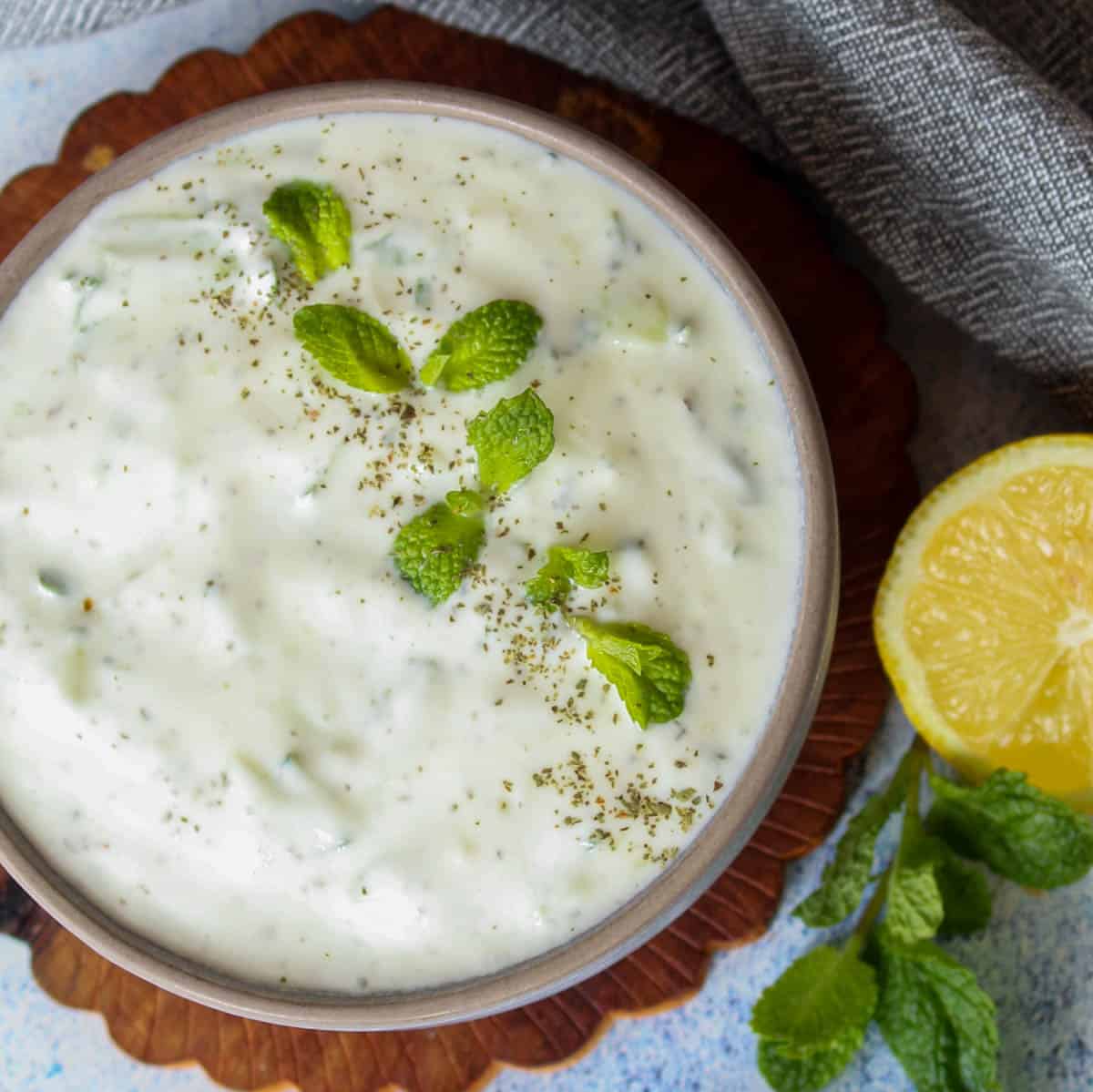 a bowl with cacik, Turkish yogurt dip, served with fresh mint leaves and slice of lemon