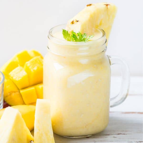 a glass jar with mango and pineapple smoothie served with fresh fruit