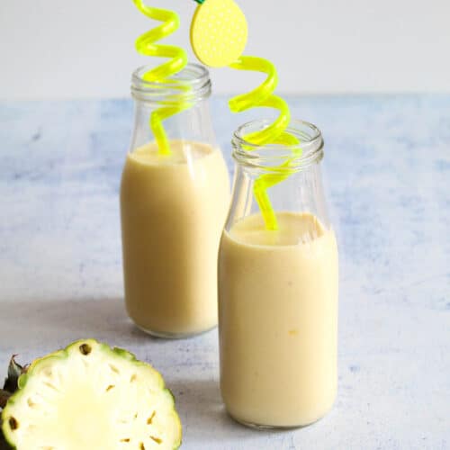 two bottles with mango pineapple smoothie with yellow straws and a pineapple slice