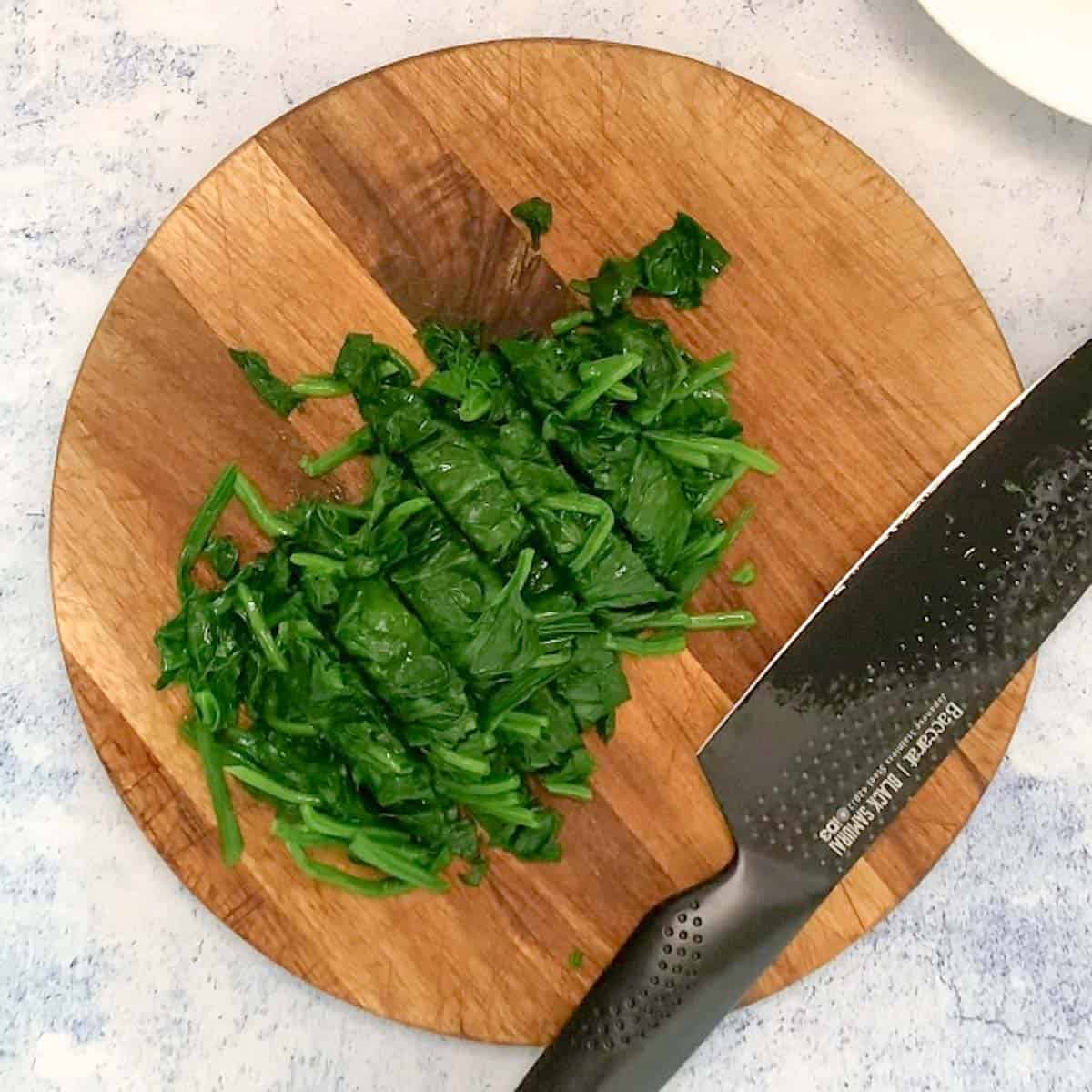 cooked spinach on a chopping board ready to be cut