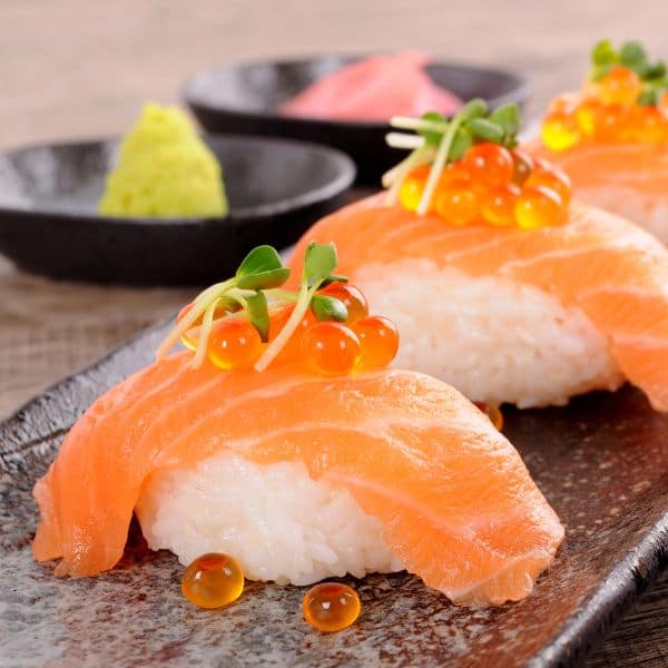 salmon nigiri beautifully presented on a plate with caviar and wasabi