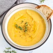 a bowl of creamy carrot and potato soup served with a slice of crusty bread