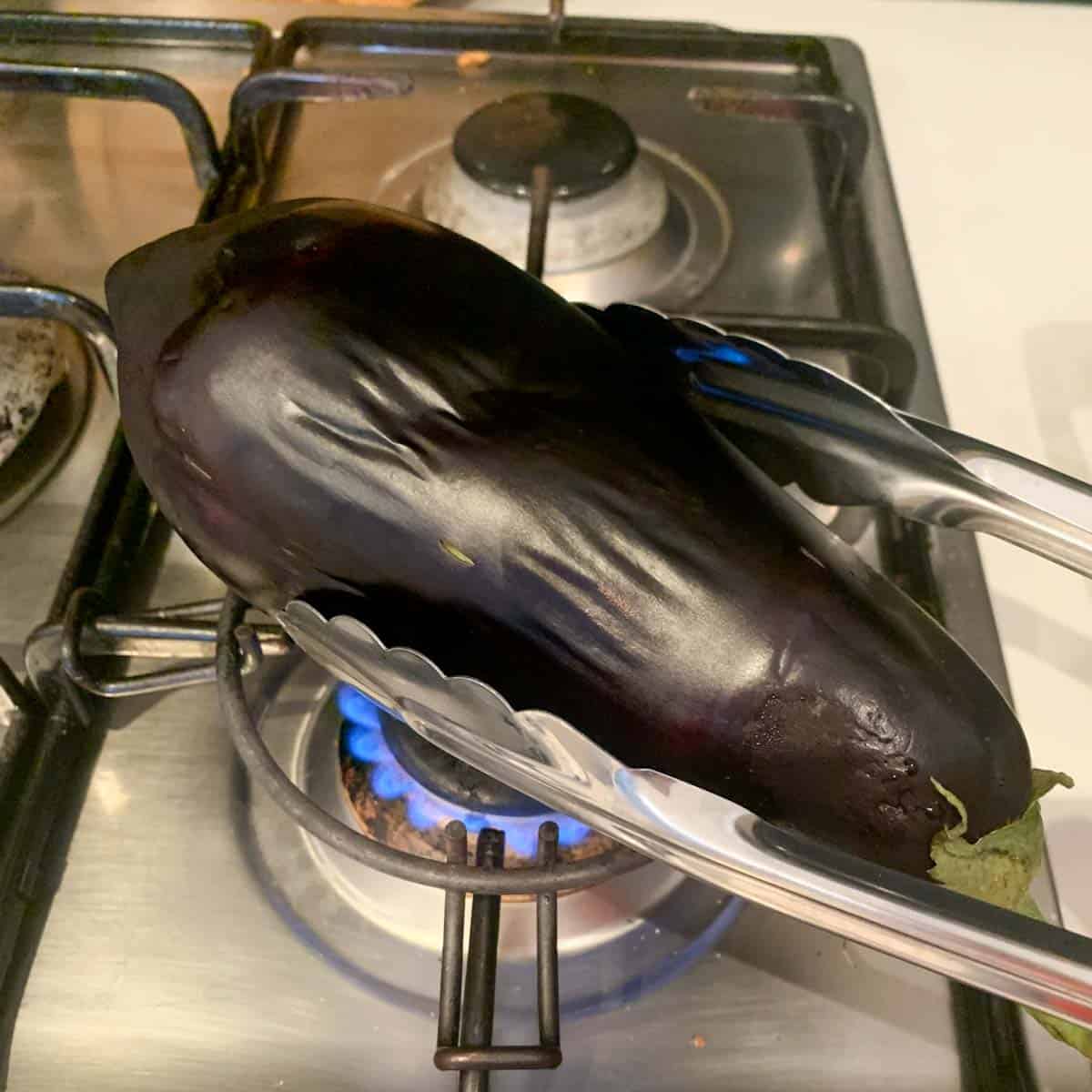 turning eggplant with kitchen tongs on a gas stove