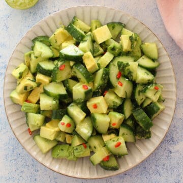 deliciously looking cucumber avocado salad on a grey plate served with fresh red chilies