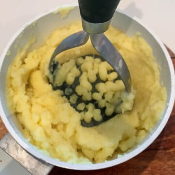 potatoes in a pan being mashed with hand potato masher