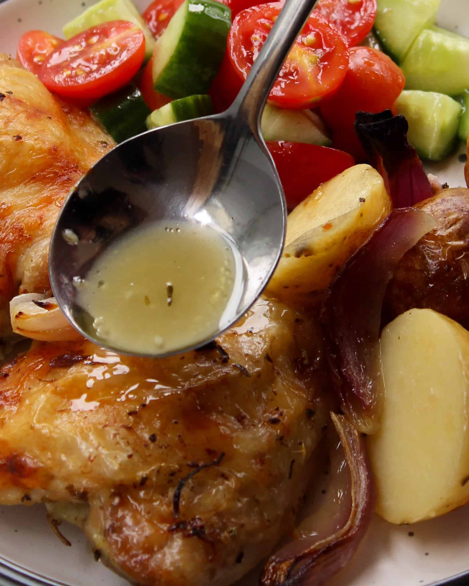 a spoon dripping the sauce onto baked golden Greek chicken thigh