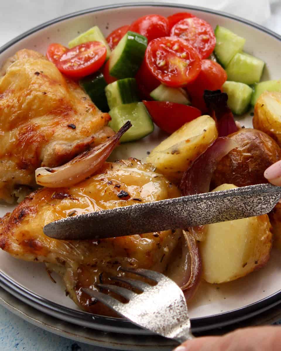 Cripsy golden Greek chicken and potatoes on a plate cut with fork and knife.