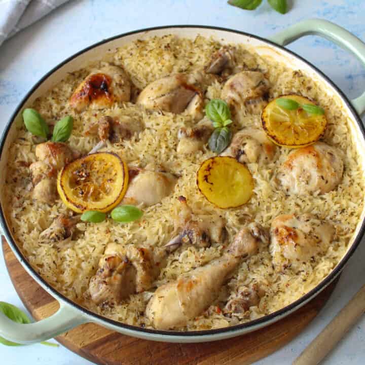 Baked Greek lemon chicken drumsticks on top of fluffy rice in a large shallow Dutch oven