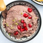 A black bowl filled with vegan black bean dip, garnished with pomegranate seeds, served with dipping ingredients.