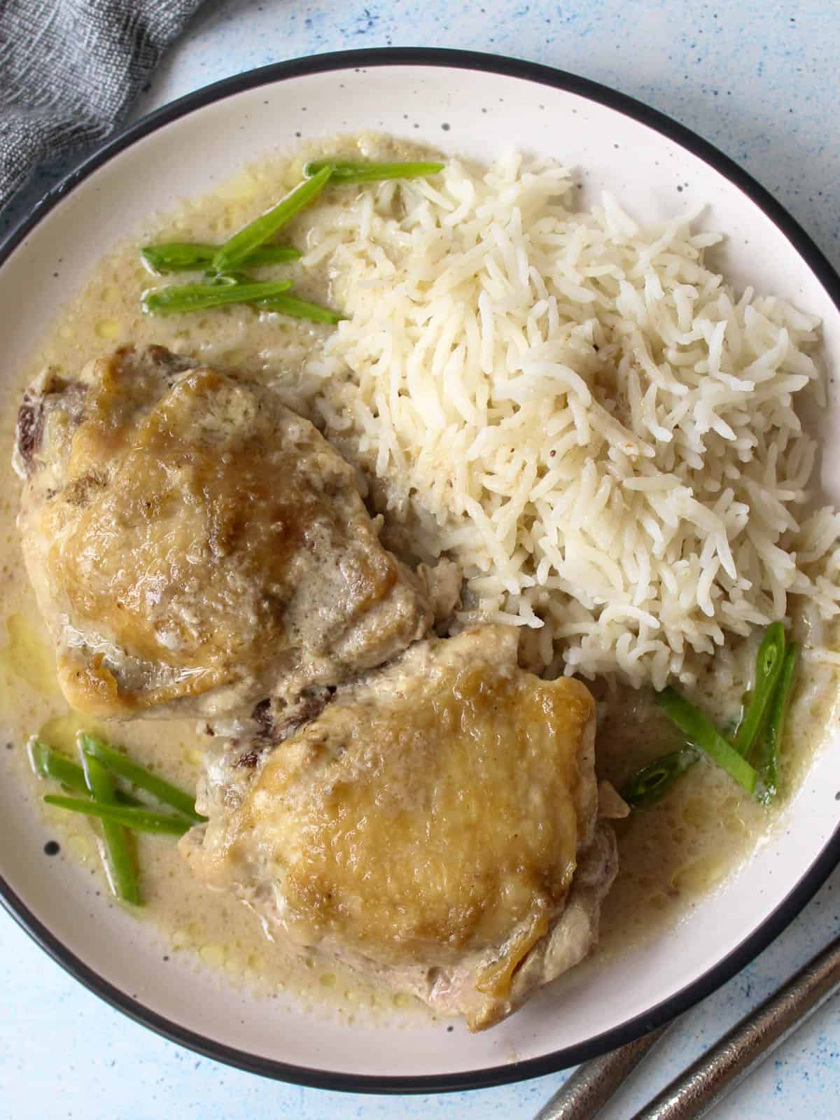 two cooked chicken thighs in green curry sauce served with basmati rice