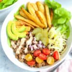 a loaded beef burger bowl with golden fries, avocado slices, cherry tomatoes, ready to be served.