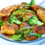 deliciously looking golden chicken thighs on a plate served with broccoli and green snow peas.