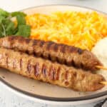 two grilled Turkish lamb kebabs served with carrots rice and cilantro leaves.